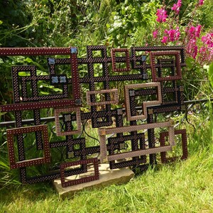 Puede incluir: Una pieza de arte de pared hecha de múltiples marcos cuadrados, cada uno con un diseño diferente. Los marcos están dispuestos en un patrón geométrico y están hechos de madera con un acabado marrón oscuro. Los marcos están decorados con pequeños tachuelas de metal.