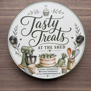 May include: A circular sign with a white background and olive green border featuring the text "Tasty Treats AT THE SHED" in a decorative script. Illustrations include a stand mixer, a cake, a piping bag, and kitchen utensils. Contact details are printed at the bottom.