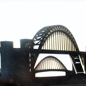 May include: Black silhouette of a city skyline with a tall church building on the left and a large arch bridge in the center.