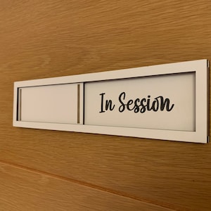 May include: A white sign with a black frame and the text "In Session" on a wooden door.