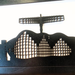 May include: Black and white silhouette of a city skyline with a large angel sculpture in the center. The sculpture is made of a grid pattern and is standing on top of a building. The skyline is made of a series of buildings with a grid pattern.