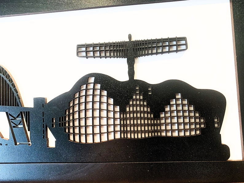May include: Black and white silhouette of a city skyline with a large angel sculpture in the center. The sculpture is made of a grid pattern and is standing on top of a building. The skyline is made of a series of buildings with a grid pattern.
