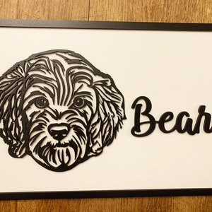 Op de afbeelding: Zwart-witte silhouet van een hondenkop met de naam "Bear" eronder geschreven in een cursief schrift. De afbeelding is ingelijst in een zwart frame.