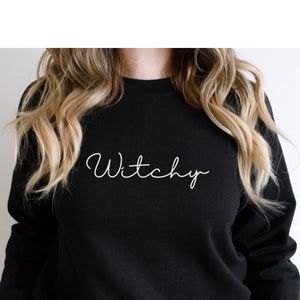 May include: Black sweatshirt with the word "Witchy" written in white cursive script.