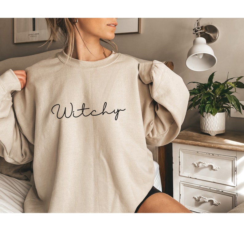 May include: A beige sweatshirt with the word "Witchy" written in black cursive script.