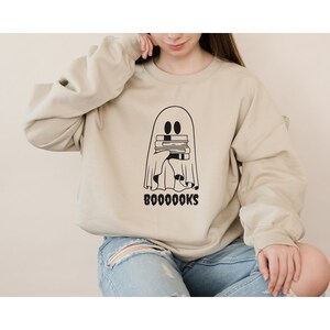 May include: A beige sweatshirt with a black ghost holding a stack of books and the text "BOO0000KS" printed on the front.