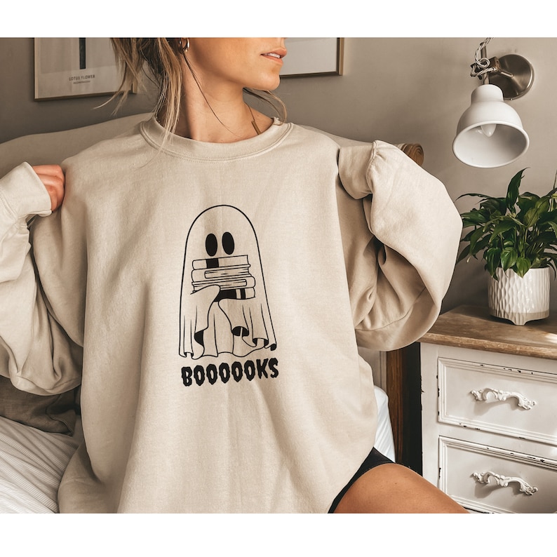 May include: A beige sweatshirt with a black ghost holding a stack of books and the text "BOOOOOKS" printed on the front.