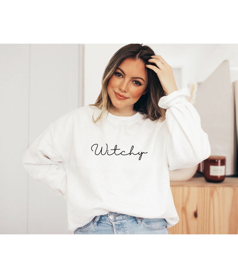 May include: White sweatshirt with the word "Witchy" written in black cursive script.