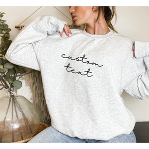 Puede incluir: Una sudadera gris con el texto "custom text" escrito en cursiva negra en la parte delantera.