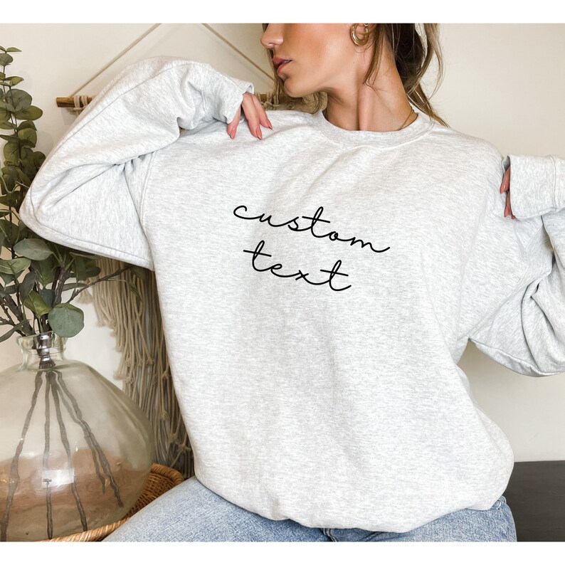 Puede incluir: Una sudadera gris con el texto "custom text" escrito en cursiva negra en la parte delantera.