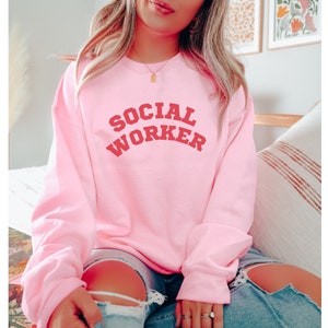 Peut inclure: Sweat-shirt rose avec le texte "SOCIAL WORKER" en rouge.
