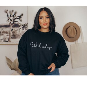 May include: Black sweatshirt with the word "Witchy" written in white cursive on the front.