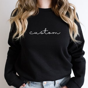 Puede incluir: Sudadera negra con la palabra "custom" escrita en letras blancas cursivas.