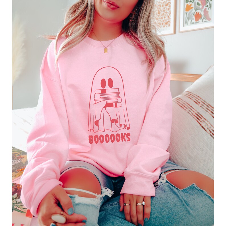 May include: A pink sweatshirt with a red ghost holding a stack of books. The text "BOO0000KS" is printed below the ghost.