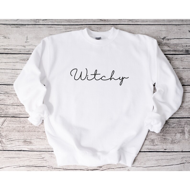 May include: White sweatshirt with the word "Witchy" written in black cursive script.