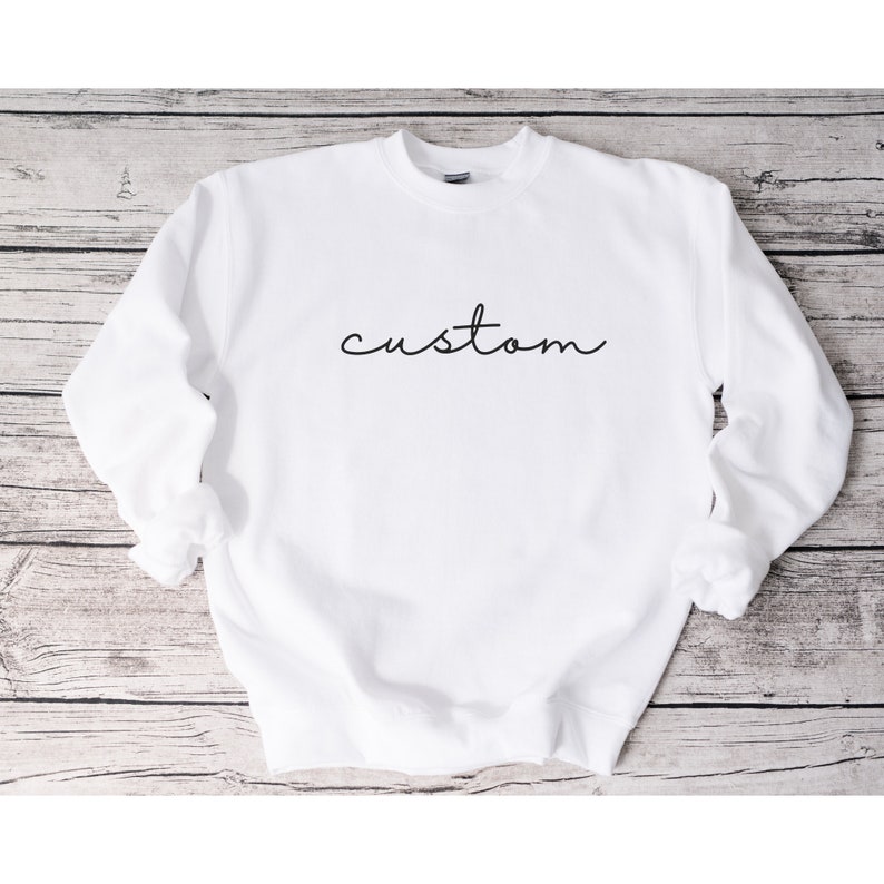 Puede incluir: Sudadera blanca de cuello redondo con la palabra "custom" escrita en cursiva negra.