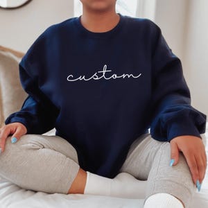 Puede incluir: Una sudadera azul marino con la palabra "custom" escrita en blanco en la parte delantera.