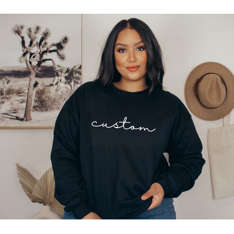 Puede incluir: Una sudadera negra con la palabra "custom" escrita en cursiva blanca.