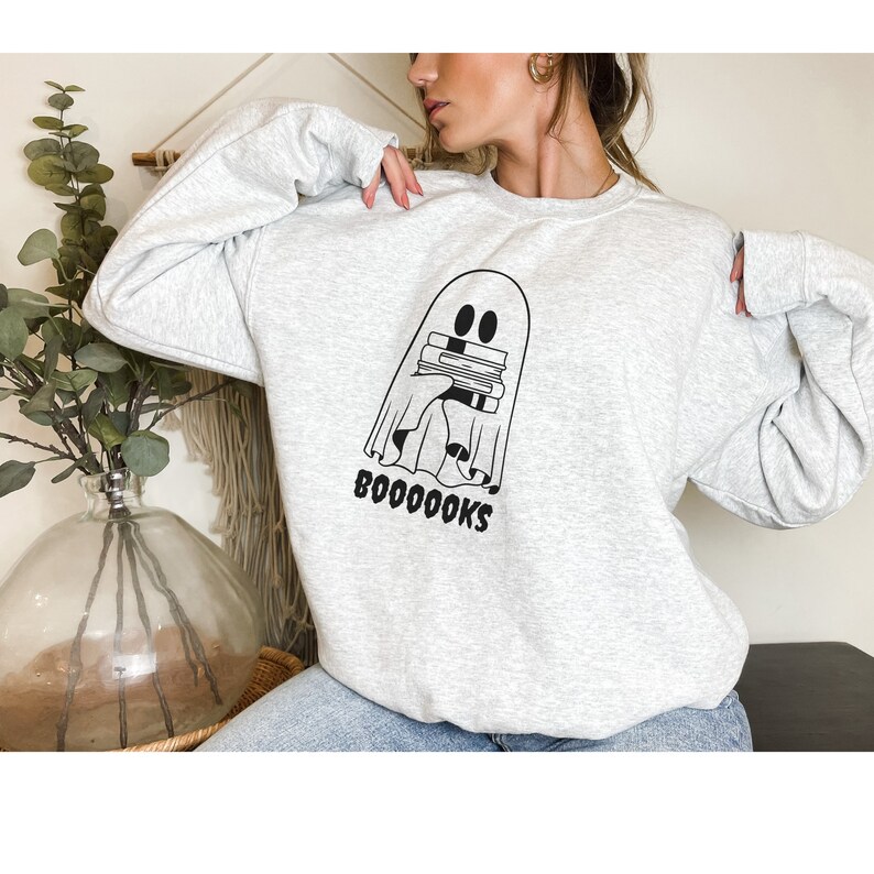 May include: A gray sweatshirt with a black graphic of a ghost holding a stack of books. The text "BOOOOOKS" is printed below the ghost.