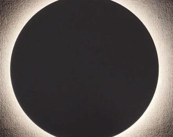 May include: A round, black wall light fixture with a white halo around the edge. The light is turned on and illuminates the wall around the fixture.