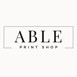 May include: Logo for Able Print Shop, featuring the word "ABLE" in a bold, serif font above "PRINT SHOP" in a smaller, sans-serif font, all within a rectangular frame. The text is black against a cream background.