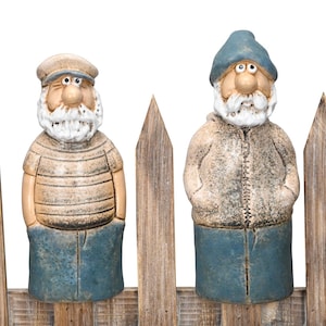 Può includere: Due gnomi da giardino in ceramica, uno con camicia a righe e berretto, l'altro con giacca con cappuccio e cappello. Entrambi hanno barbe bianche e pantaloni blu, dietro una staccionata di legno. Una decorazione esterna stravagante.