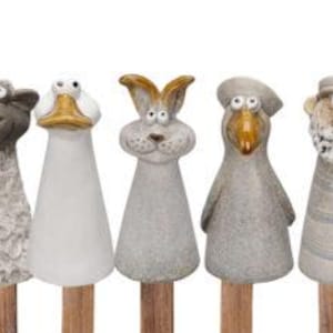 Op de afbeelding: Vijf keramische tuinpalen met dierengezichten. De palen zijn in verschillende kleuren geverfd, waaronder grijs, wit en bruin. De dieren zijn een schaap, een eend, een konijn, een vogel en een man met een baard.