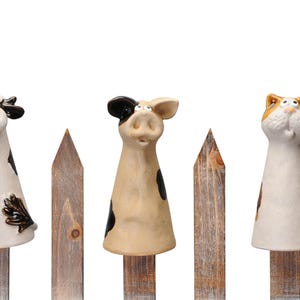 Può includere: Quattro figurine di animali in ceramica, una mucca, un maiale e un gatto, sono appollaiate su pali di legno di una recinzione. Le figurine sono dipinte di bianco, nero, marrone e arancione.