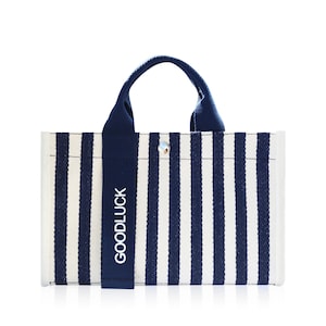 May include: A white and navy blue striped tote bag with a navy blue handle and the word "GOODLUCK" printed on the handle.