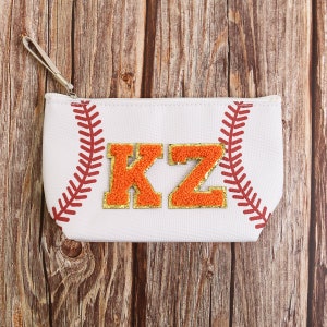 Puede incluir: Bolsa con cremallera blanca con tem&aacute;tica de b&eacute;isbol con detalles de costura rojos. Presenta las letras "KZ" de chenilla naranja y dorada. Incluye una peque&ntilde;a correa para la mu&ntilde;eca. La bolsa est&aacute; sobre un fondo de madera.