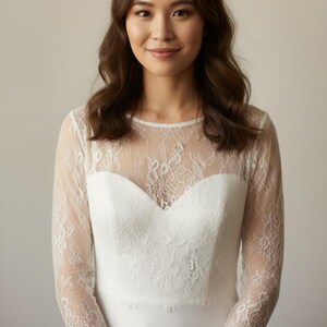 Bride wearing a white lace top with long sheer sleeves, styled as a wedding dress topper lace bolero shrug and floral lace blouse for wedding.