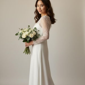 Bride wearing a white lace top with long sheer sleeves, styled as a wedding dress topper lace bolero shrug and floral lace blouse for wedding.