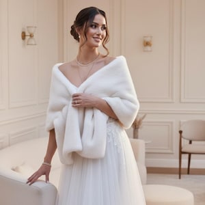 Bridal fur wedding shawl styled as a faux fur wrap, cape, or stole for dress. Elegant white bridal shrug and wedding dress cover up for a cozy winter ceremony look.