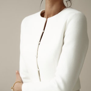 May include: A white cropped jacket with long sleeves and a button closure. The jacket is made of a soft, smooth fabric.