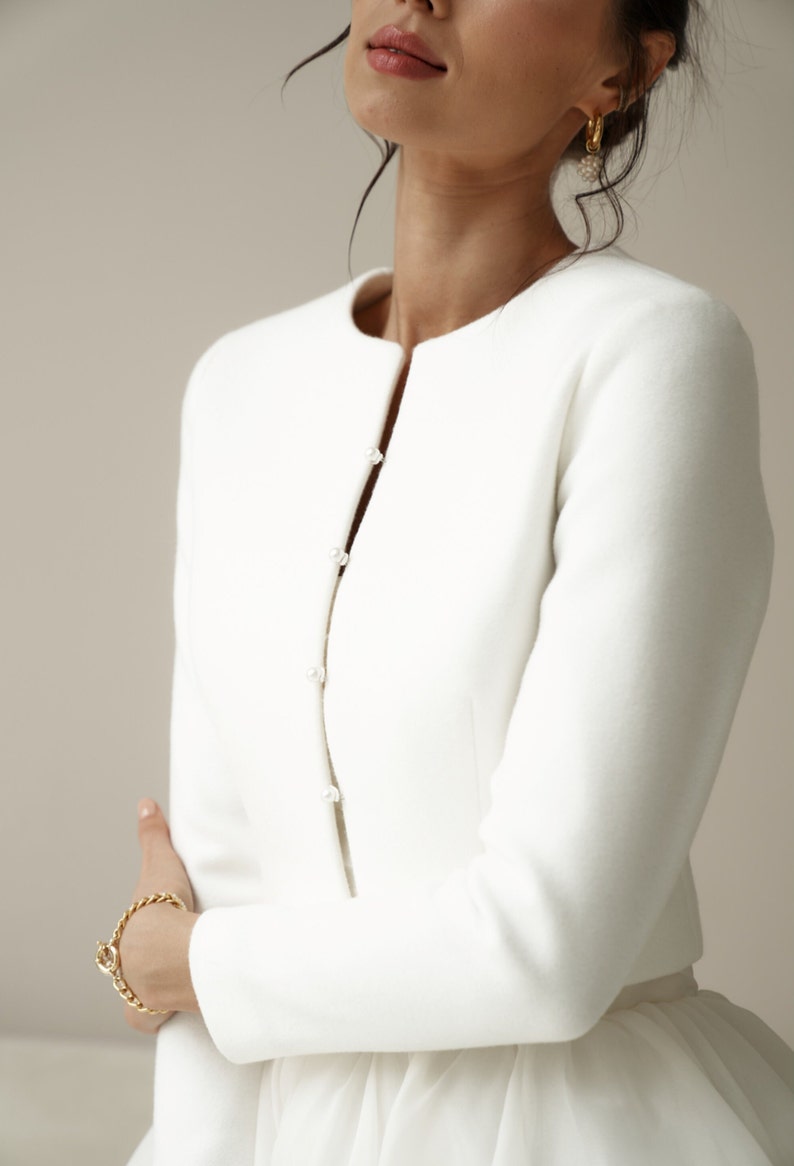 May include: A white cropped jacket with long sleeves and a button closure. The jacket is made of a soft, smooth fabric.
