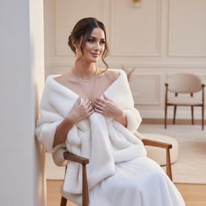 Bridal fur wedding shawl styled as a faux fur wrap, cape, or stole for dress. Elegant white bridal shrug and wedding dress cover up for a cozy winter ceremony look.