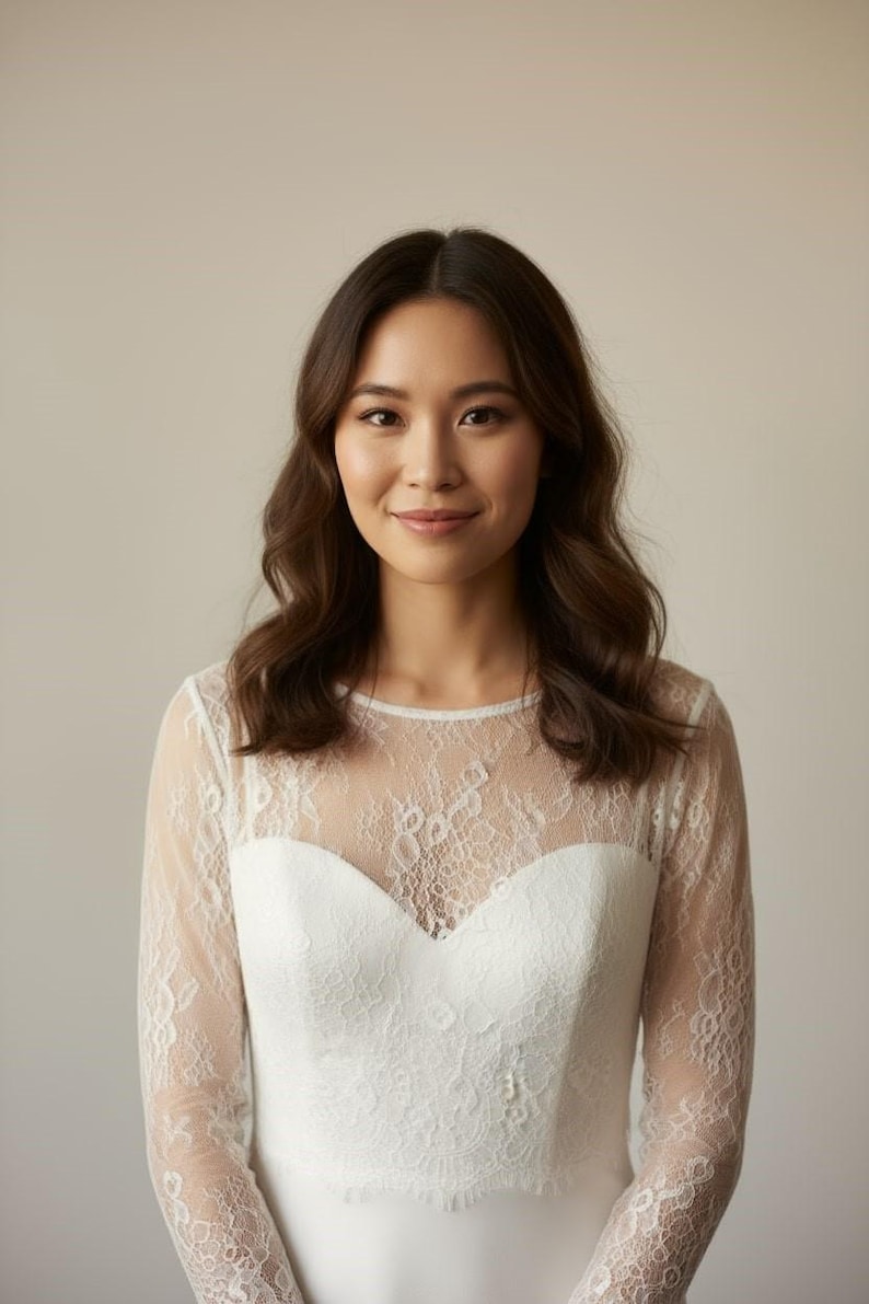 Bride wearing a white lace top with long sheer sleeves, styled as a wedding dress topper lace bolero shrug and floral lace blouse for wedding.