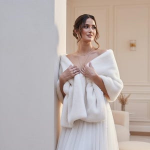 Bridal fur wedding shawl styled as a faux fur wrap, cape, or stole for dress. Elegant white bridal shrug and wedding dress cover up for a cozy winter ceremony look.
