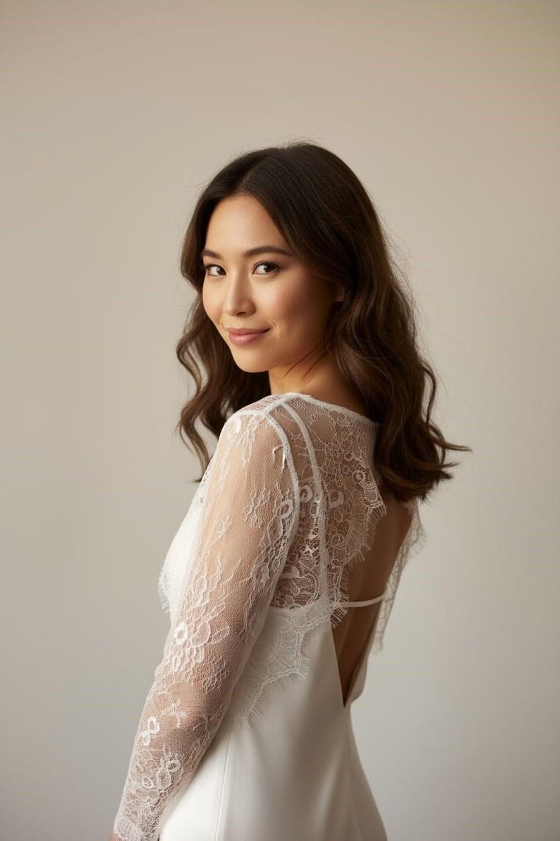 Bride wearing a white lace top with long sheer sleeves, styled as a wedding dress topper lace bolero shrug and floral lace blouse for wedding.
