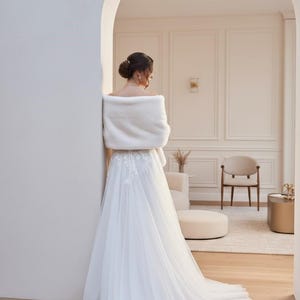 Bridal fur wedding shawl styled as a faux fur wrap, cape, or stole for dress. Elegant white bridal shrug and wedding dress cover up for a cozy winter ceremony look.