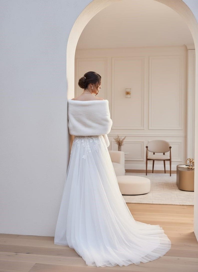 Bridal fur wedding shawl styled as a faux fur wrap, cape, or stole for dress. Elegant white bridal shrug and wedding dress cover up for a cozy winter ceremony look.