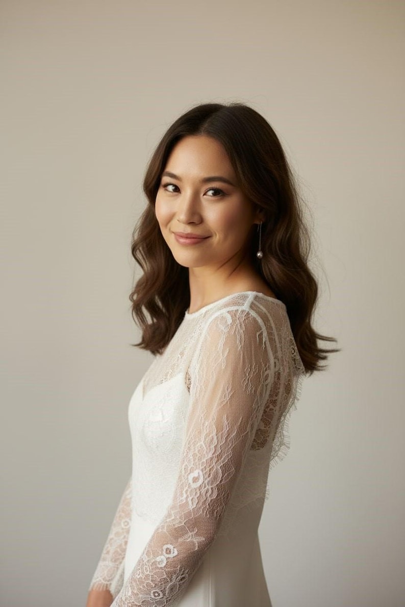 Bride wearing a white lace top with long sheer sleeves, styled as a wedding dress topper lace bolero shrug and floral lace blouse for wedding.