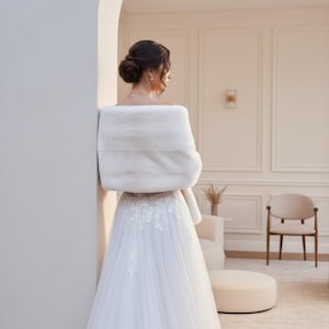 Bridal fur wedding shawl styled as a faux fur wrap, cape, or stole for dress. Elegant white bridal shrug and wedding dress cover up for a cozy winter ceremony look.