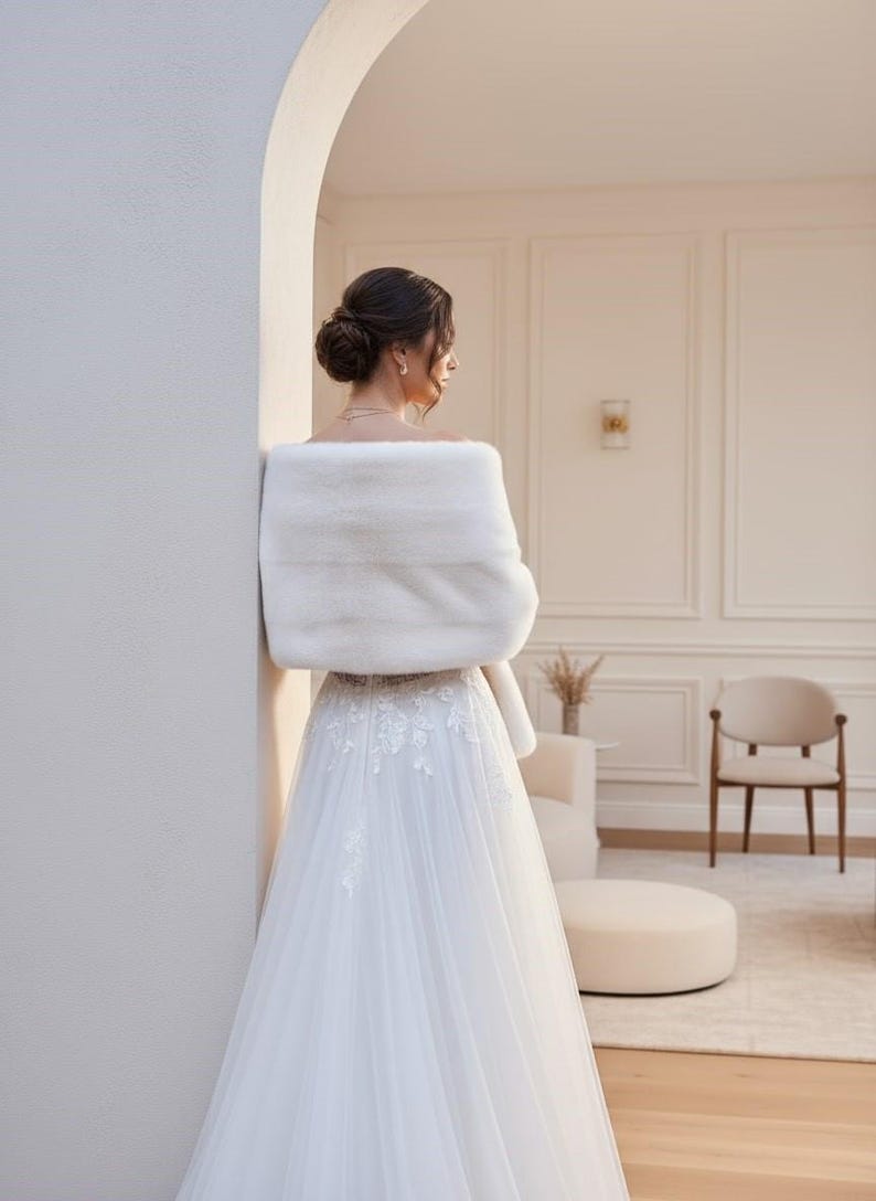Bridal fur wedding shawl styled as a faux fur wrap, cape, or stole for dress. Elegant white bridal shrug and wedding dress cover up for a cozy winter ceremony look.