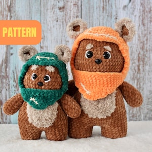 Könnte beinhalten: Zwei gehäkelte Plüschtiere in Form eines braunen Ewoks mit einem flauschigen Gesicht und großen Ohren. Der größere Ewok trägt einen orangefarbenen Kapuzen-Schal und der kleinere Ewok trägt einen grünen Kapuzen-Schal. Die Spielzeuge stehen auf einer weißen Oberfläche.