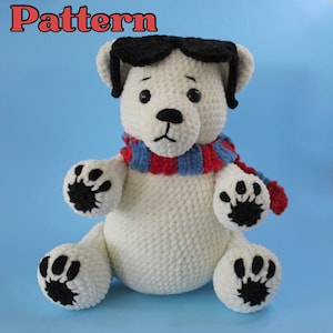 Peut inclure: Un ours en crochet blanc fait à la main portant des lunettes de soleil noires et une écharpe rayée bleue, rouge et blanche. L'ours a des coussinets noirs et le mot "Pattern" est écrit en rouge en haut.