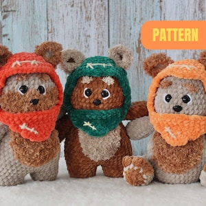 Könnte beinhalten: Drei gehäkelte Plüschtiere, die Ewoks aus Star Wars ähneln. Die Spielzeuge sind braun mit flauschigem Fell und haben große, runde Ohren. Jedes Spielzeug trägt eine gehäkelte Kapuze in einer anderen Farbe: orange, grün und orange. Die Spielzeuge sitzen auf einer weißen Oberfläche. Der Text "PATTERN" ist in Gelb auf orangefarbenem Hintergrund geschrieben.
