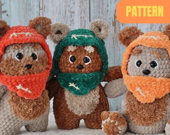 May include: Three crocheted plush toys resembling Ewoks from Star Wars. The toys are brown with fuzzy fur and have large, round ears. Each toy is wearing a crocheted hood in a different color: orange, green, and orange. The toys are sitting on a white surface. The text "PATTERN" is written in yellow on an orange background.