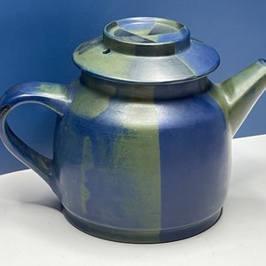 May include: A ceramic teapot with a lid, featuring a blue and green color scheme. The teapot has a handle and a spout. The lid has a geometric design. The teapot is likely used for brewing tea and is a decorative kitchen item.