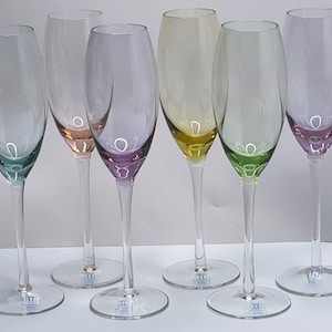 May include: Six clear glass champagne flutes with colored bases. The bases are in shades of green, yellow, pink, and blue.